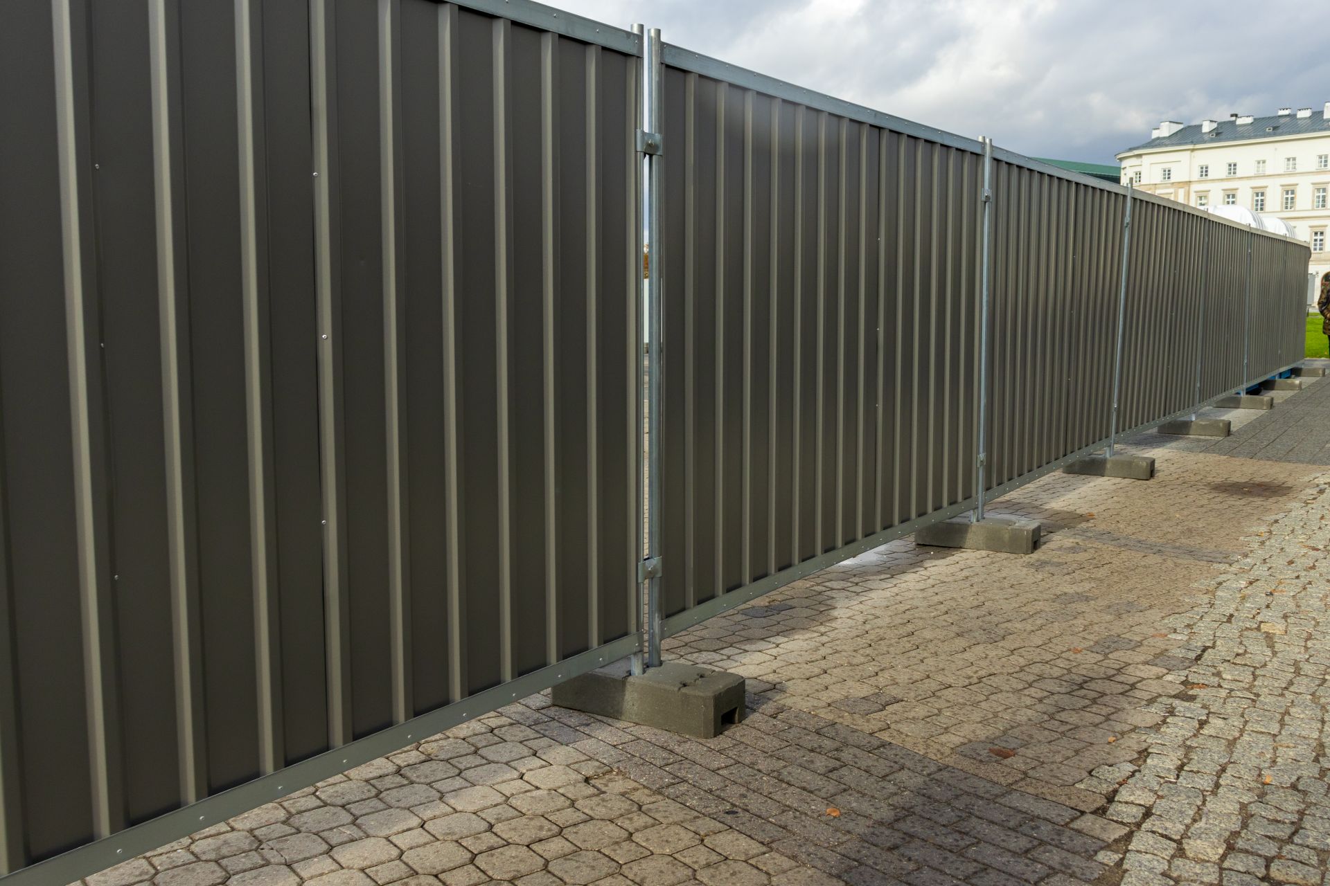 Mobile Schallschutzwand aus Metallpaneelen mit Betonfüßen auf öffentlicher Fläche vor Gebäude