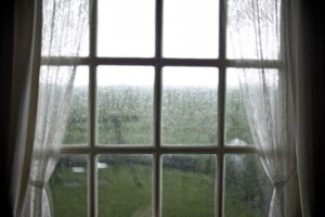 Fenster mit Regentropfen und Vorhaengen, Symbol fuer Nachhaltigkeit und bewusste Regenwassernutzung im Alltag