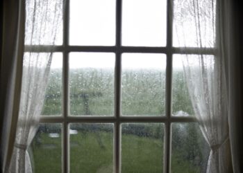 Fenster mit Regentropfen und Vorhaengen, Symbol fuer Nachhaltigkeit und bewusste Regenwassernutzung im Alltag