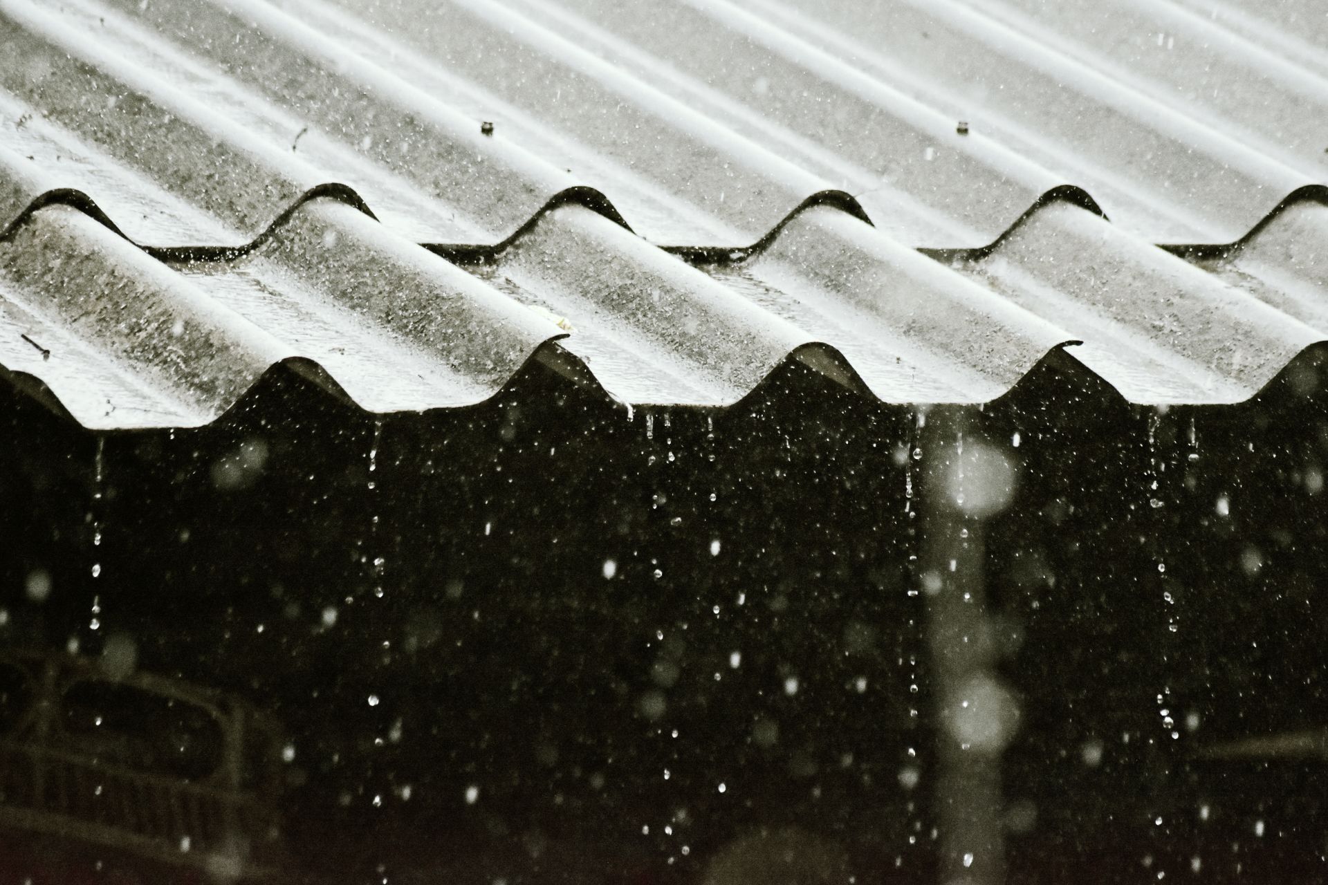 Regen tropft von einem Dach mit Blechplatten, Symbol fuer den Beginn der Regenwassernutzung am Haus