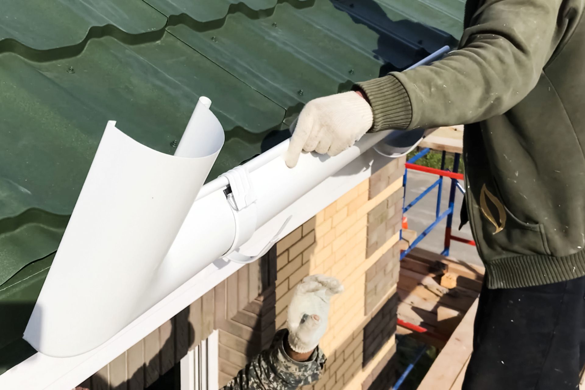 Handwerker installiert weisse Dachrinne an gruenem Hausdach als Teil eines Systems zur Regenwassernutzung
